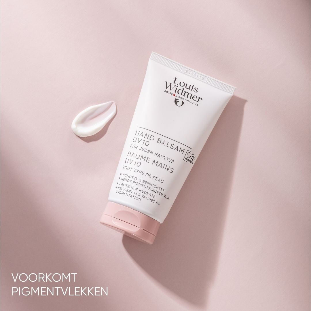 Witte tube met productnaam en logo. Tekst: Hand Balsam UV10, 0% Parfum. Op roze achtergrond. Klodder crème ernaast.
