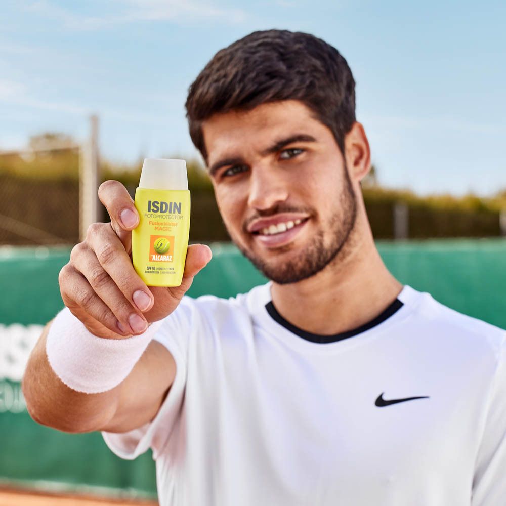 Homme tenant un flacon jaune. Inscription: ISDIN Fotoprotector Fusion Water MAGIC. Logo balle de tennis.