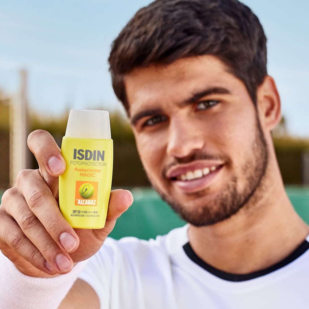 Man houdt gele fles vast. Opschrift: ISDIN Fotoprotector Fusion Water MAGIC. Tennisbal-logo.