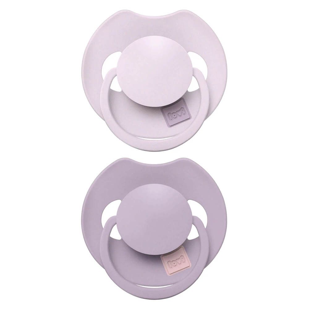 Deux sucettes lilas. Elles ont toutes deux une tétine ronde et un anneau. Le nom de la marque est visible.