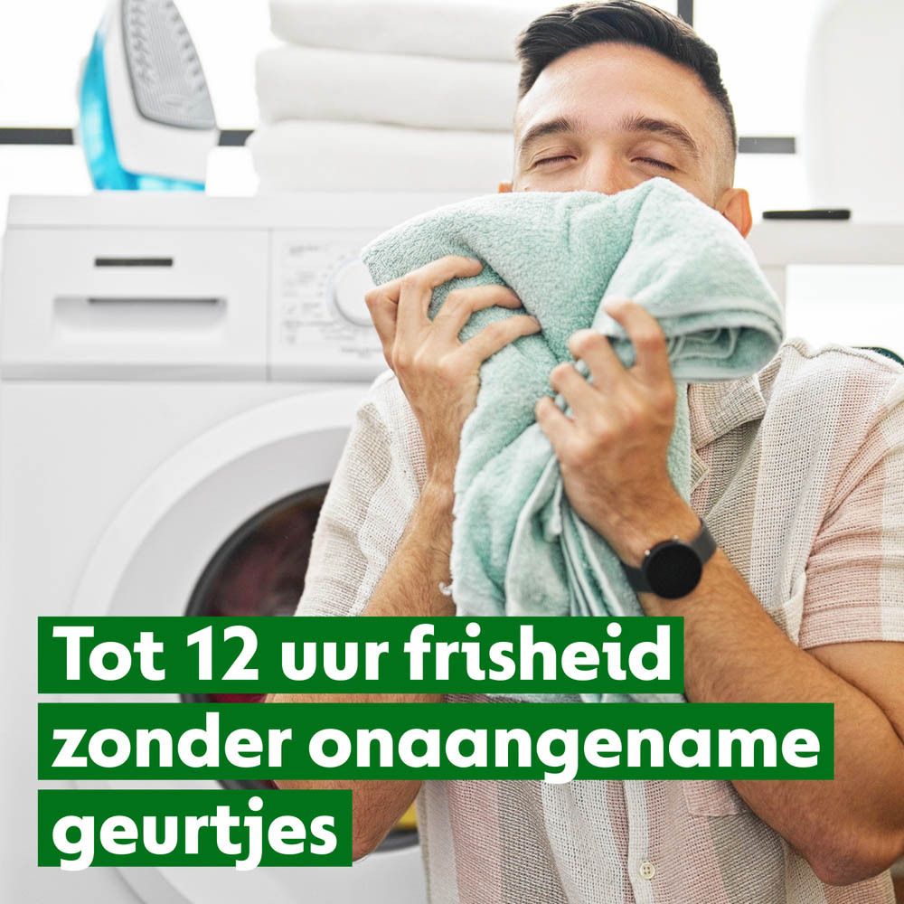 Man ruikt aan handdoek. Wasmachine op de achtergrond. Tekst: Tot 12 uur frisheid zonder onaangename geurtjes (Tot 12 uur frisheid).