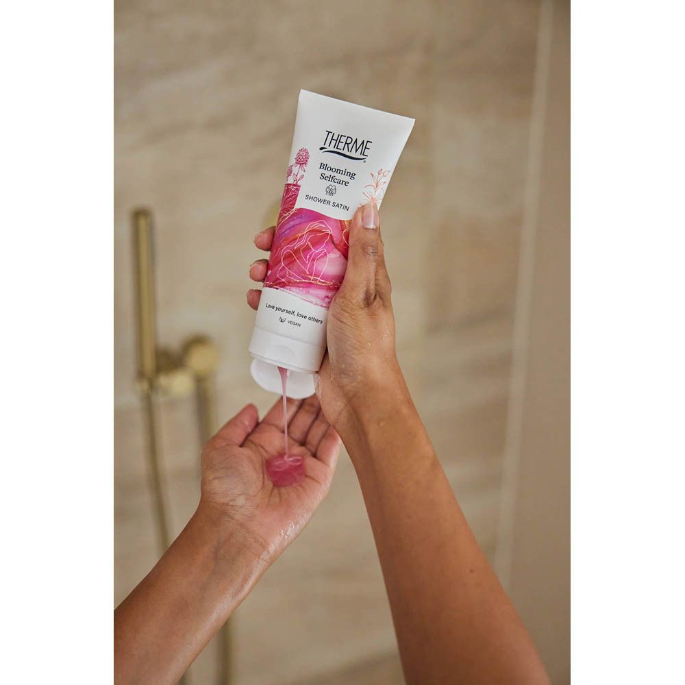 Mains tenant un tube. Le produit est pressé du tube. Douche en arrière-plan.