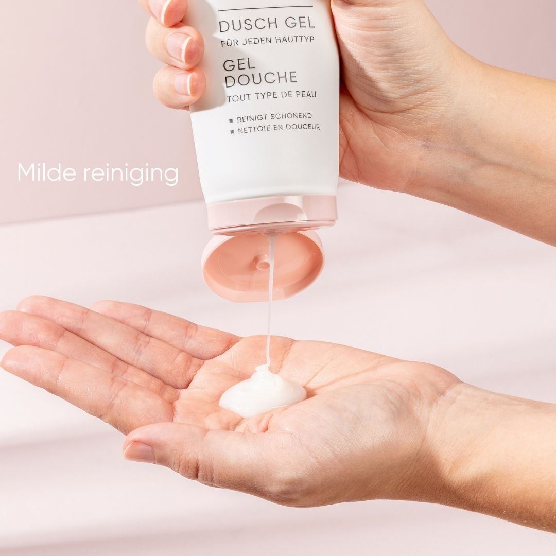 Hand houdt tube, douchegel wordt eruit geperst. Witte vloeistof. Roze achtergrond.