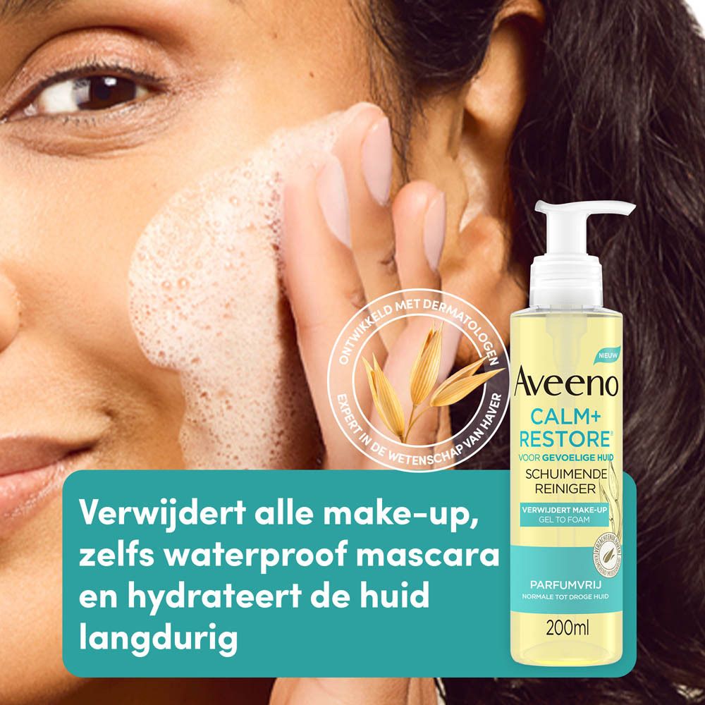 Vrouw wast gezicht met Aveeno Calm+Restore Schuimende Reiniger. Fles op de achtergrond.