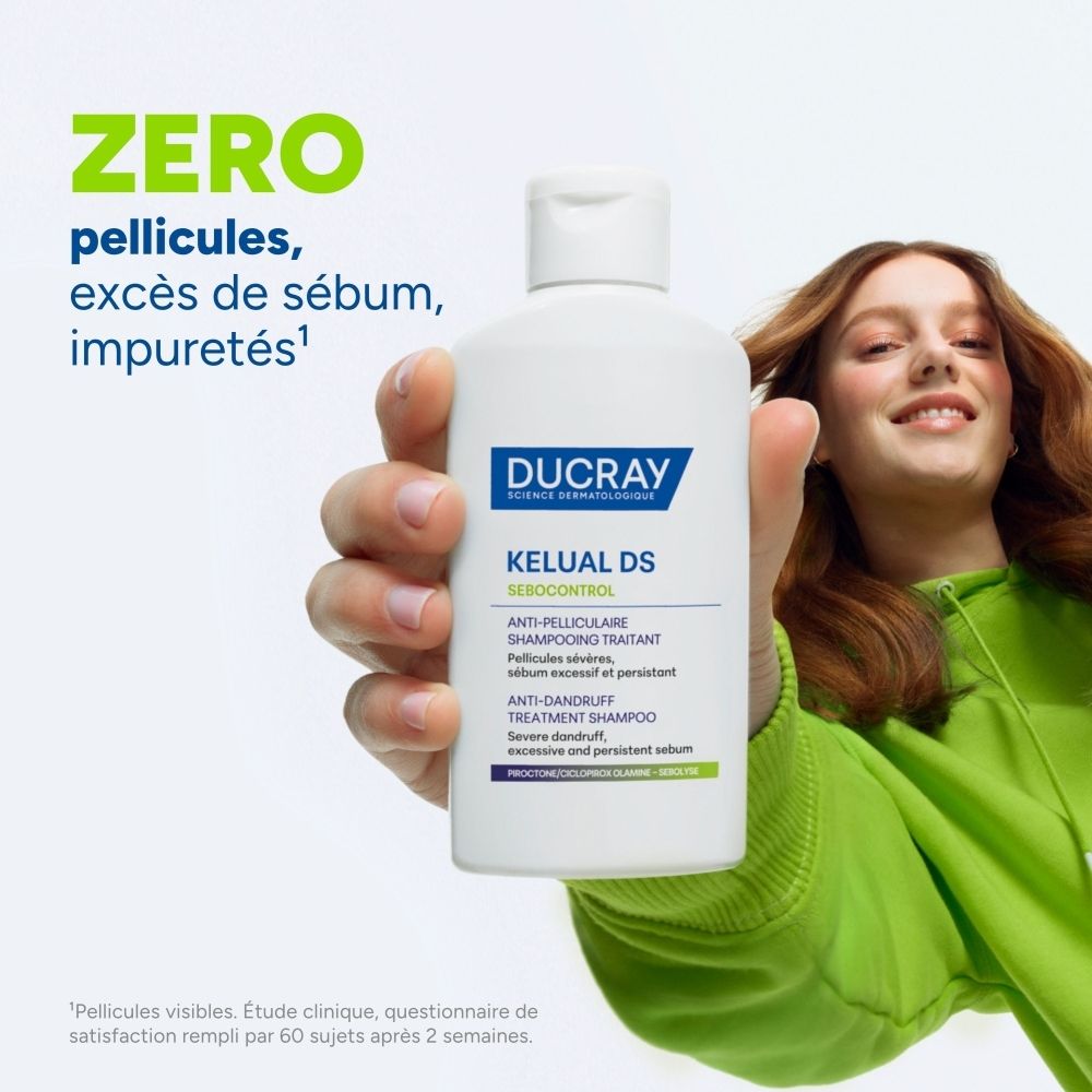 Shampooing Ducray Kelual DS : Bouteille blanche tenue dans la main d'une personne, avec du texte sur l'absence de pellicules et le contrôle du sébum.