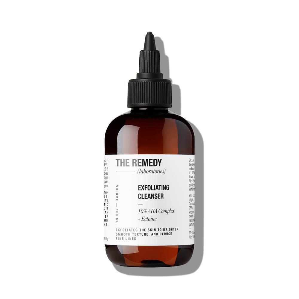 Bruine fles met zwarte dop. Etiket met productinformatie. "THE REMEDY" en "Exfoliating Cleanser" zichtbaar.