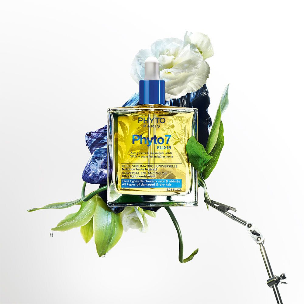 Glazen fles met gele vloeistof, omringd door bloemen. Blauwe dop met pipet. Opschrift: Phyto Paris, Phyto7 Elixir.