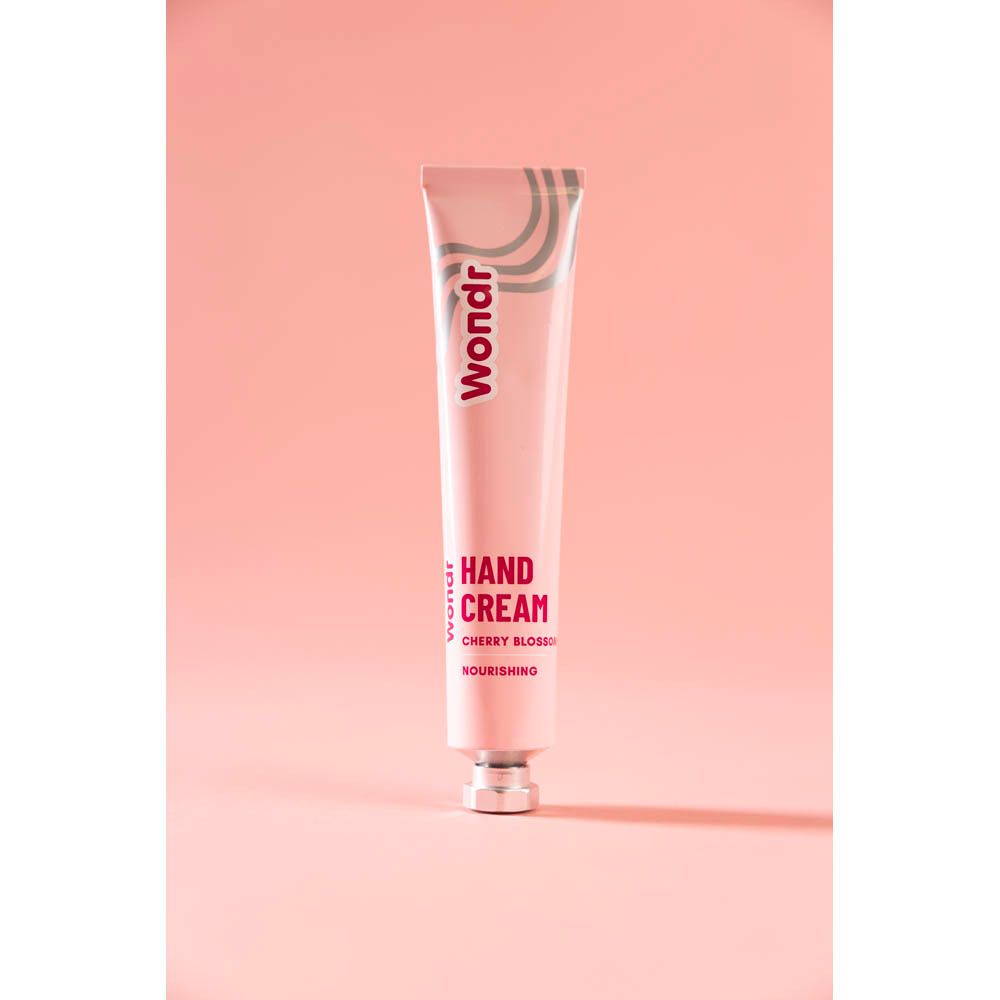 Roze tube met zilveren golven en "Wondr" logo. "Hand Cream Cherry Blossom" en "Nourishing" gedrukt.