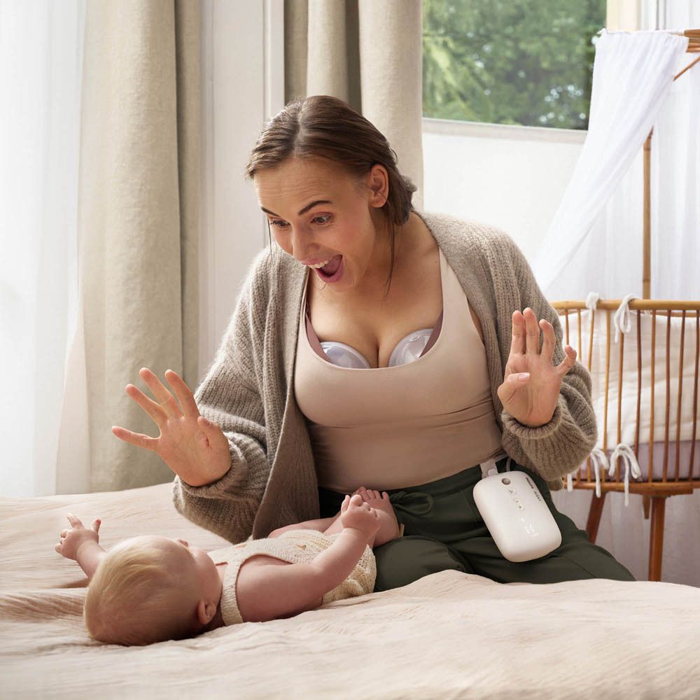 Vrouw met Philips AVENT borstkolf. Ze kijkt verrast naar haar baby. Borstkolfcomponenten zichtbaar.