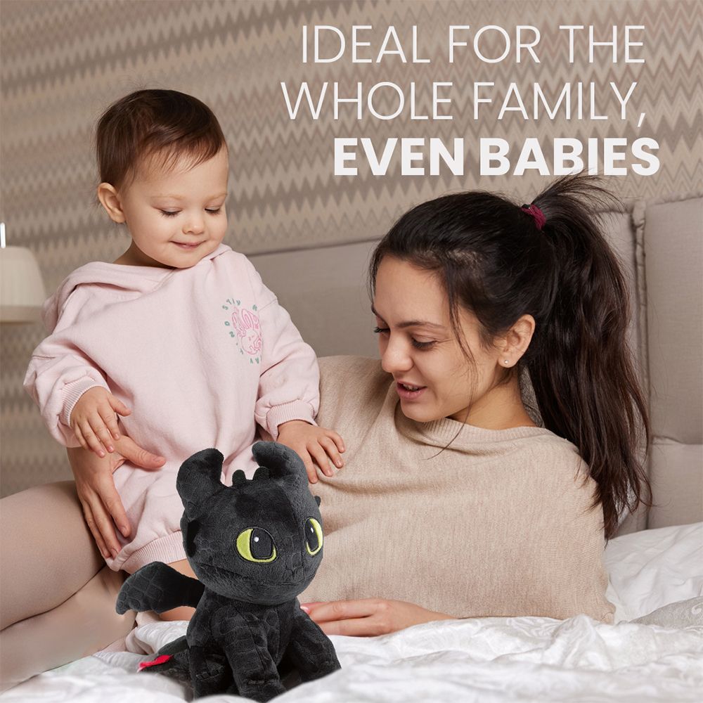 Zwarte pluche draak met baby en vrouw op een bed.