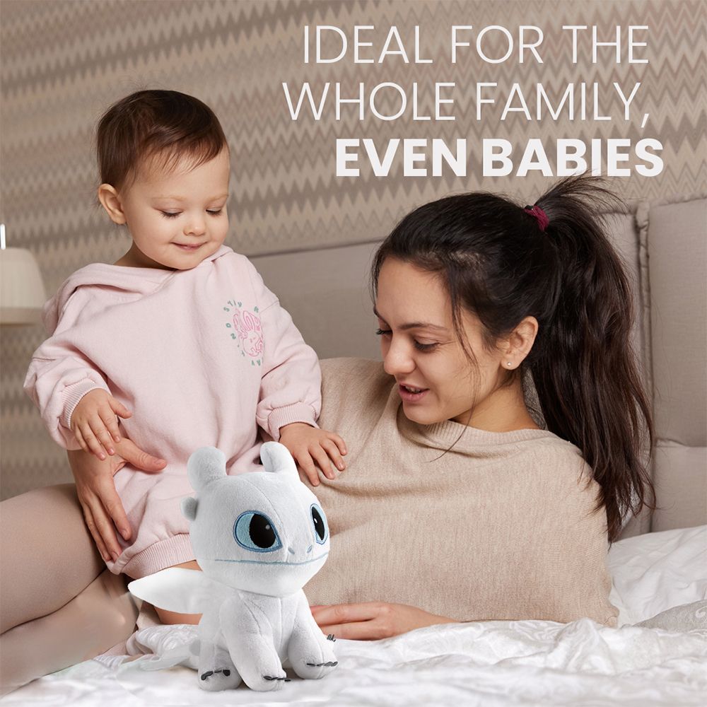 Vrouw met baby knuffelt met witte pluche draak op een bed.