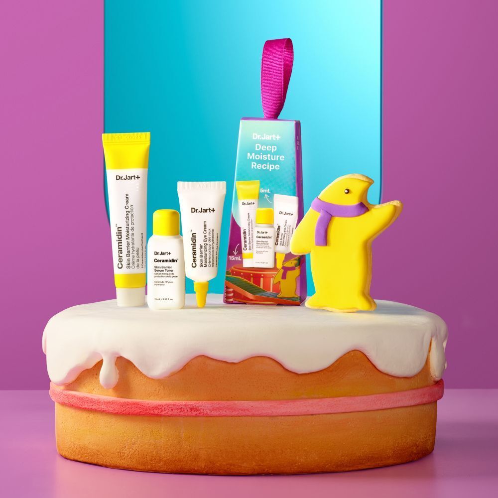 Coffret cadeau de soins de la peau sur un gâteau. Comprend des crèmes et un emballage avec un ruban violet. Inscription : Dr. Jart+ Deep Moisture Recipe.