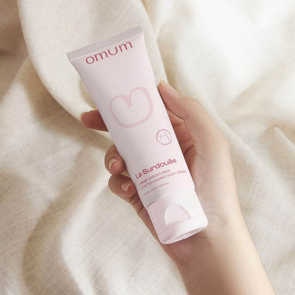 Roze tube met witte opdruk. Bovenin staat "omum". Daaronder "La Surdouée Crème Vergetures".