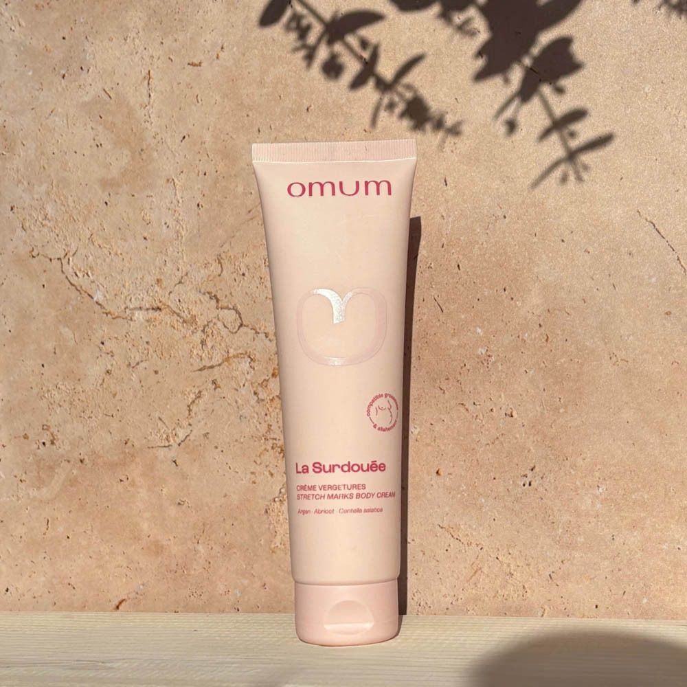 Roze tube op houten plank met bloemen. Bovenin staat "omum". Daaronder "La Surdouée Crème Vergetures".