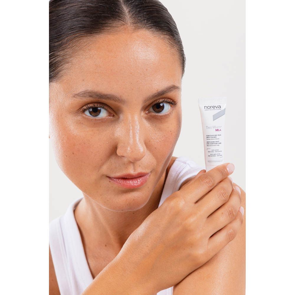 Vrouw die een tube Noreva Trio White Mela oogcontourcrème vasthoudt.