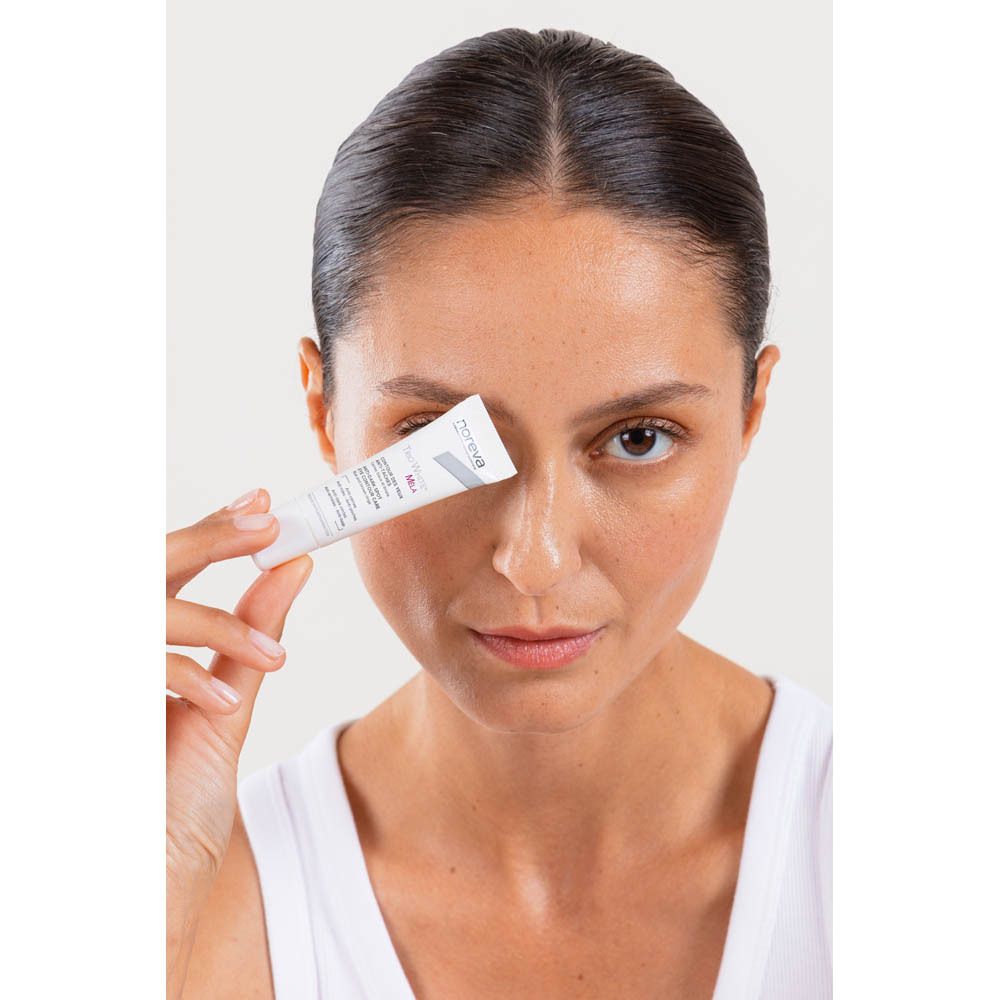 Vrouw die een tube Noreva Trio White Mela oogcontourcrème bij haar oog houdt.