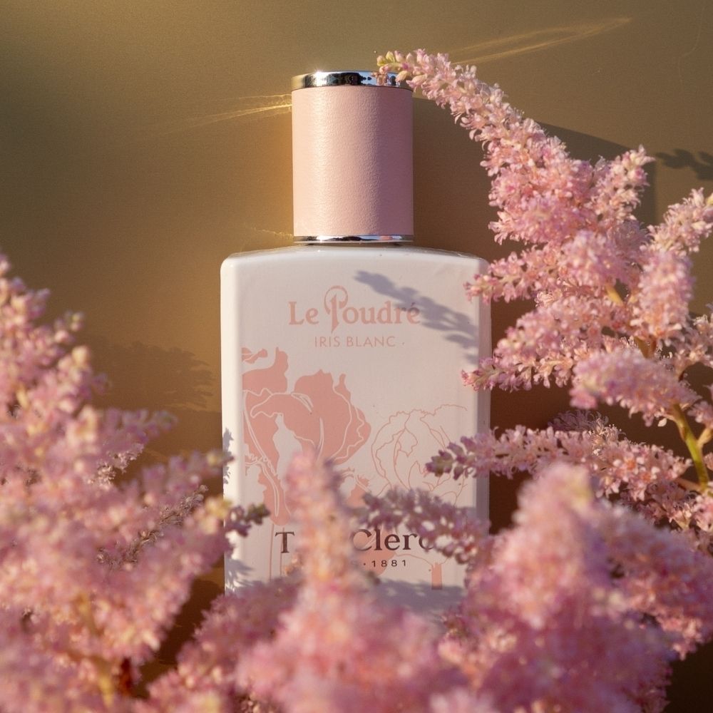 Flacon T. LeClerc Le Poudré Iris Blanc Eau de Parfum, entouré de fleurs roses.