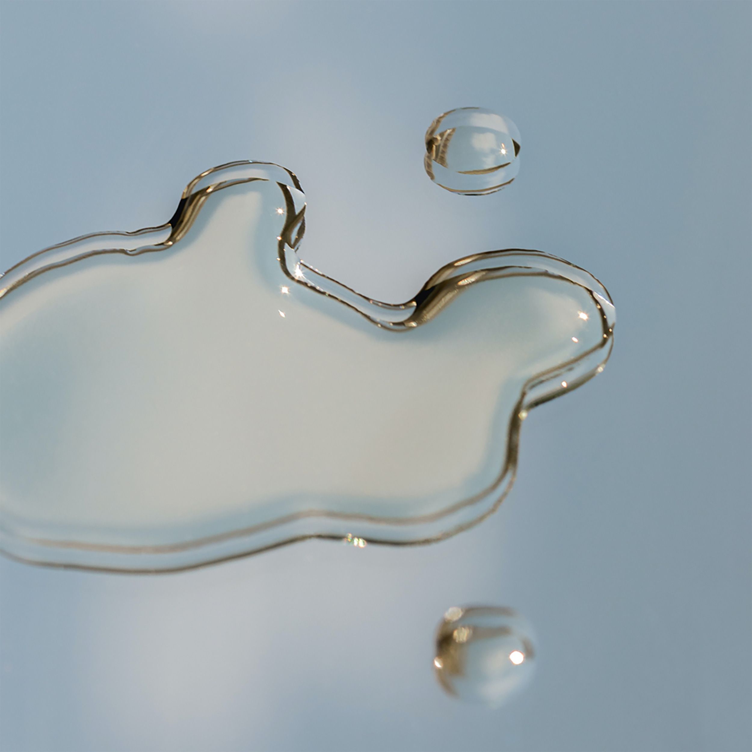 Drie druppels vloeistof op een lichtblauwe ondergrond. Ronde en onregelmatige vormen. Transparante vloeistof.