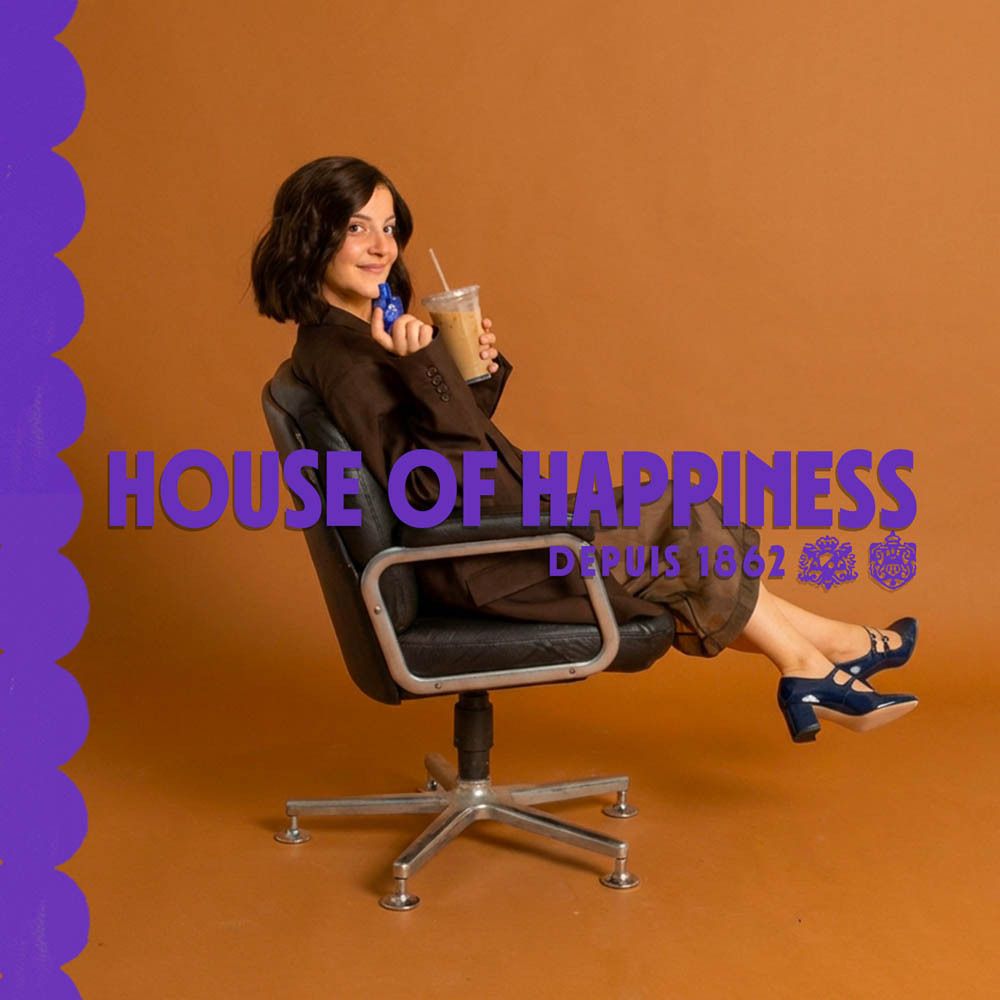 Vrouw zit met koffie en roll-on parfum. Tekst: House of Happiness, Depuis 1862.
