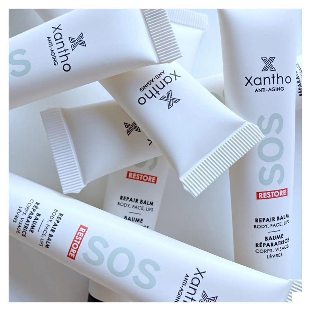 Meerdere witte tubes "SOS Restore Repair Balm" met "xantho" logo. Tekst in het Engels en Frans. Voor lippen, gezicht, lichaam.