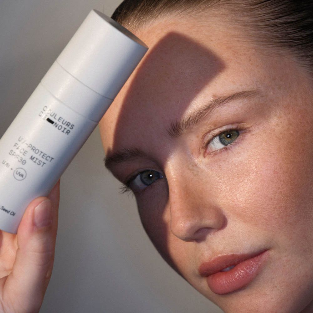 Flacon pulvérisateur blanc avec inscription 'COULEURS DE NOIR UV-PROTECT FACE MIST SPF30'.