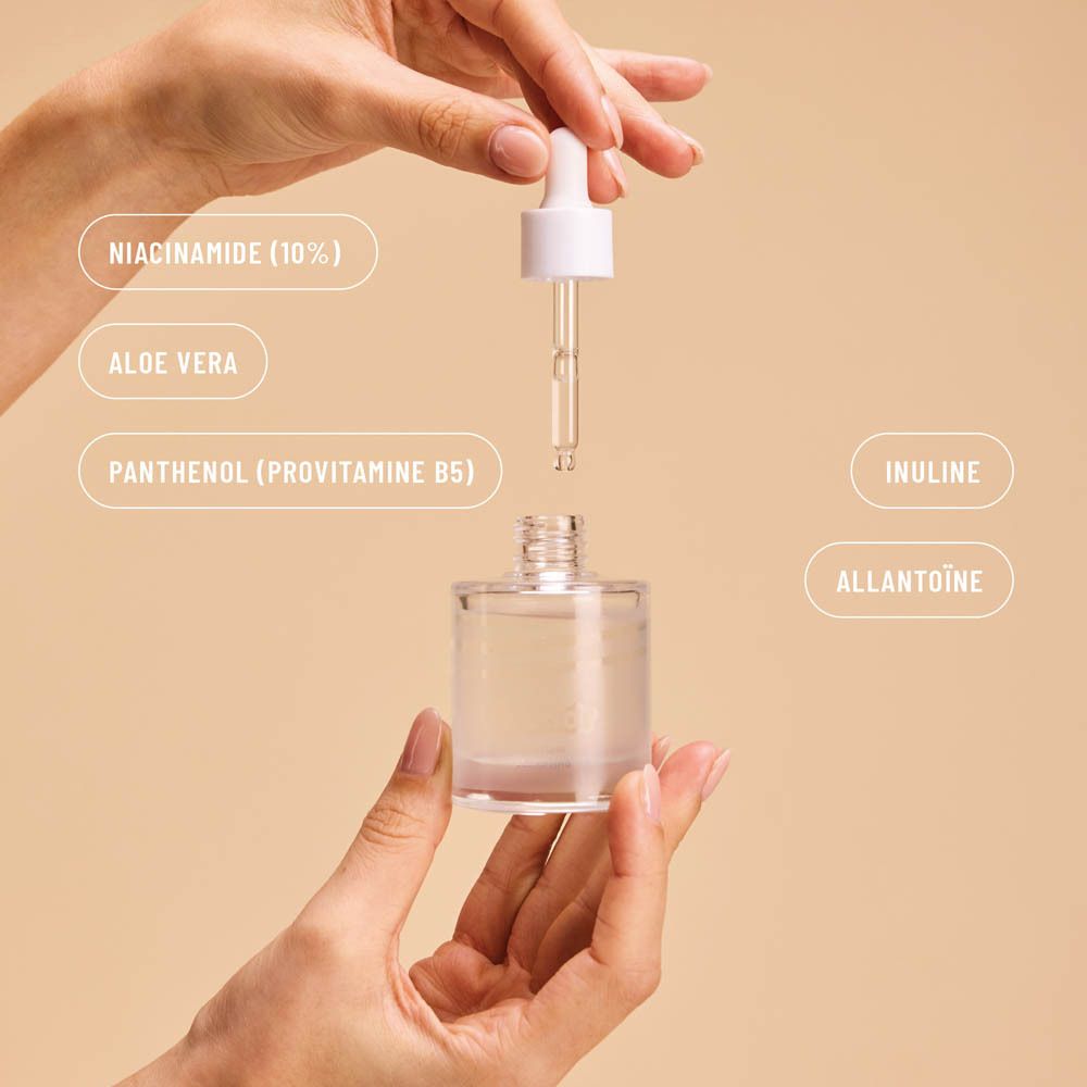 Handen houden een serumfles met pipet. Labels: Niacinamide, Aloë Vera, Panthenol, Inuline, Allantoïne.