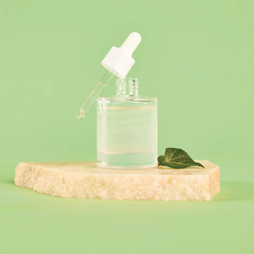 Flacon de sérum avec pipette sur pierre. Environnement vert. Logo WONDR sur le flacon.