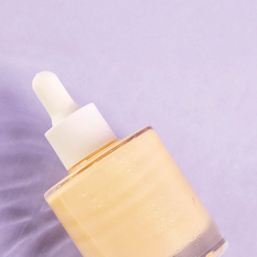 Vrouw houdt serumfles vast. Pipet met gele vloeistof. Tekst: Vitamine C, Groene thee, Q10.