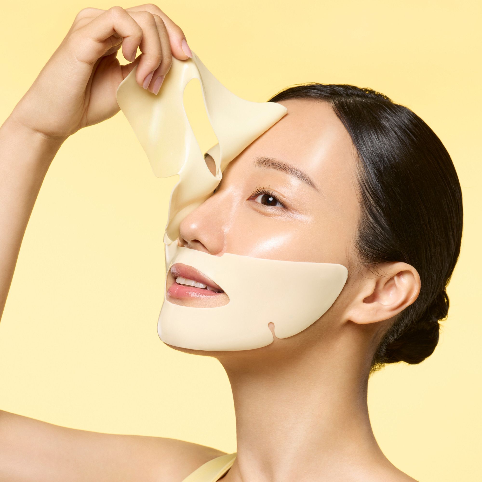 Een vrouw houdt een geel maskerblad van Dr.Jart+ Cryo Rubber™ Brightening Mask tegen haar gezicht.