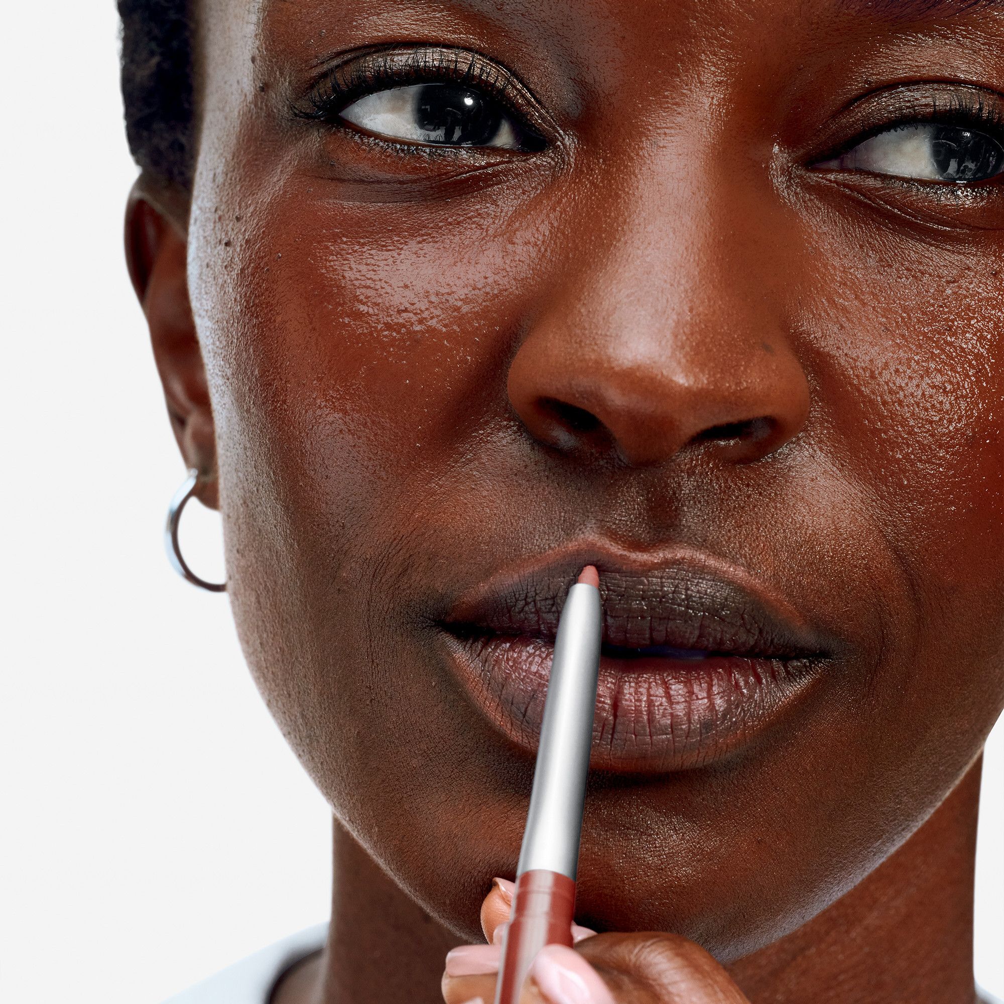 Gros plan d'une femme qui se dessine les lèvres avec un crayon à lèvres brun. Le crayon à lèvres est de Clinique.