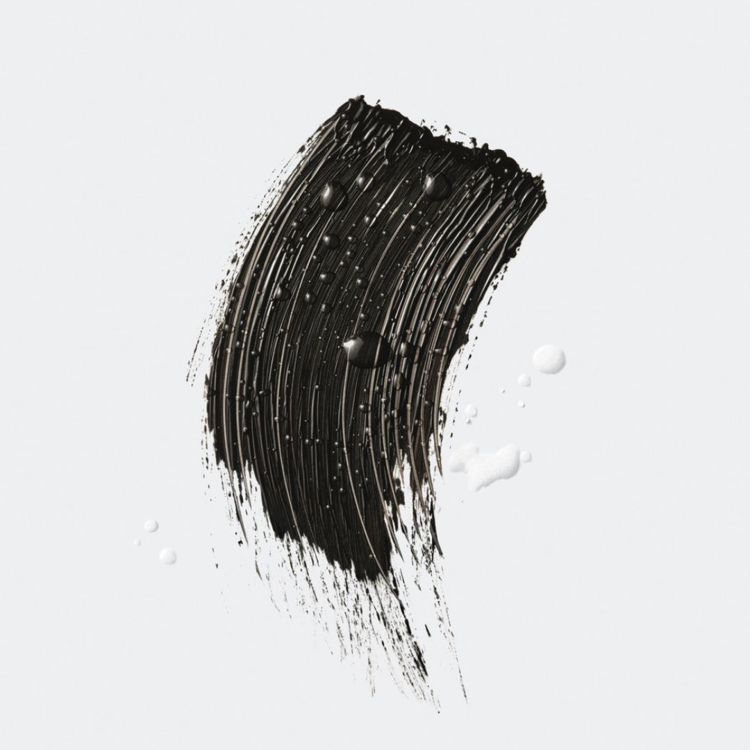 Trait de mascara noir avec gouttes d'eau. Texte: Waterproof, Volume maximum.