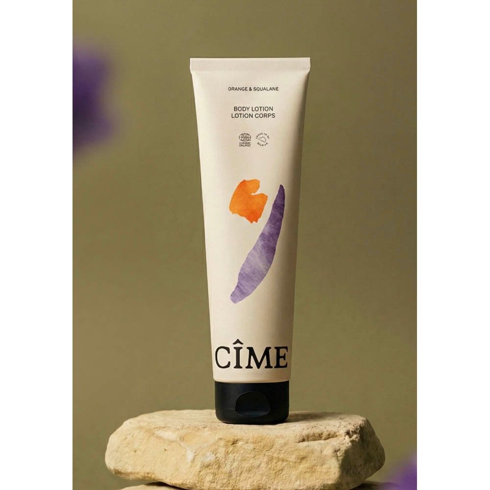 Tube de lotion pour le corps Cime sur pierre. Tube beige avec bouchon noir. Formes abstraites orange et violet. Inscription Cime.