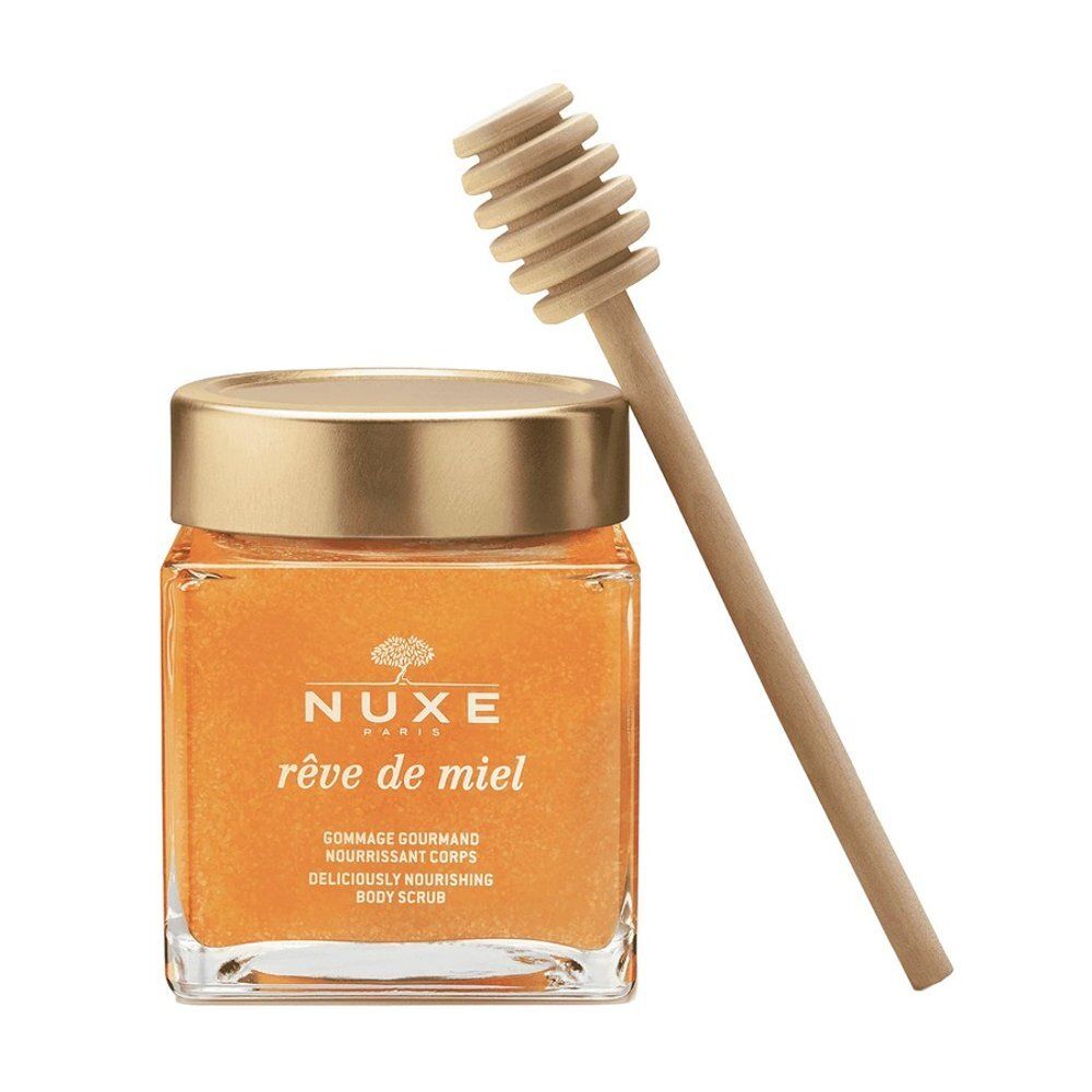 Glazen pot met gouden deksel, gevuld met oranje bodyscrub. Een houten honinglepel ligt ernaast.
