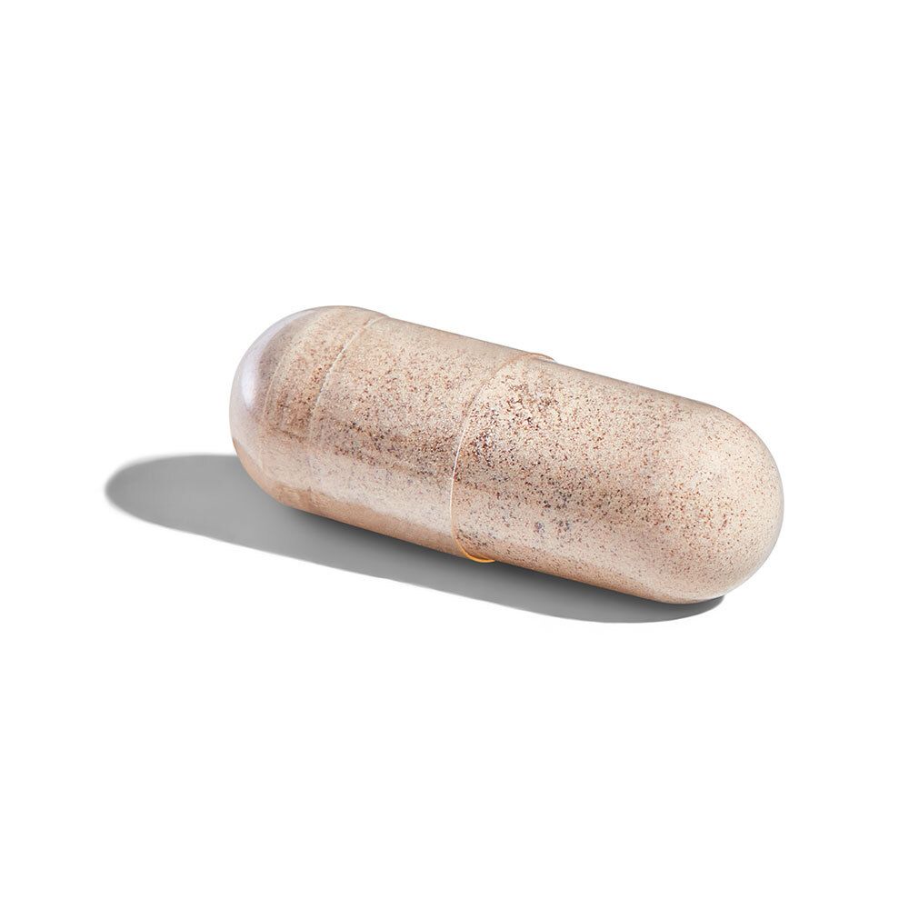 Une seule gélule beige avec des extrémités transparentes. Elle est posée sur une surface blanche.