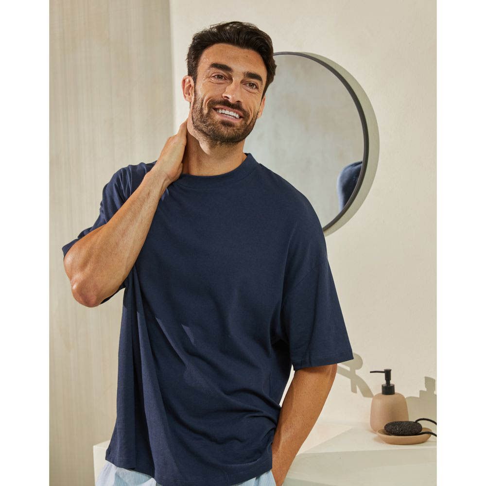Man in badkamer, glimlachend. Draagt blauw T-shirt, spiegel op de achtergrond.