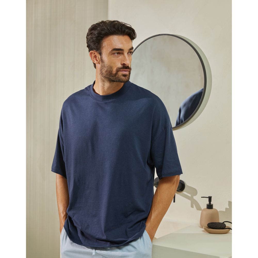 Man in badkamer, glimlachend. Draagt blauw T-shirt, spiegel op de achtergrond.