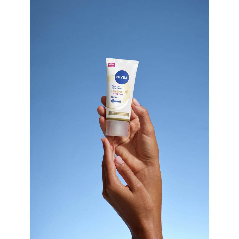 Handen van een persoon met een dot NIVEA® handcrème op de rug van de hand, naast een kopje koffie op een dienblad.