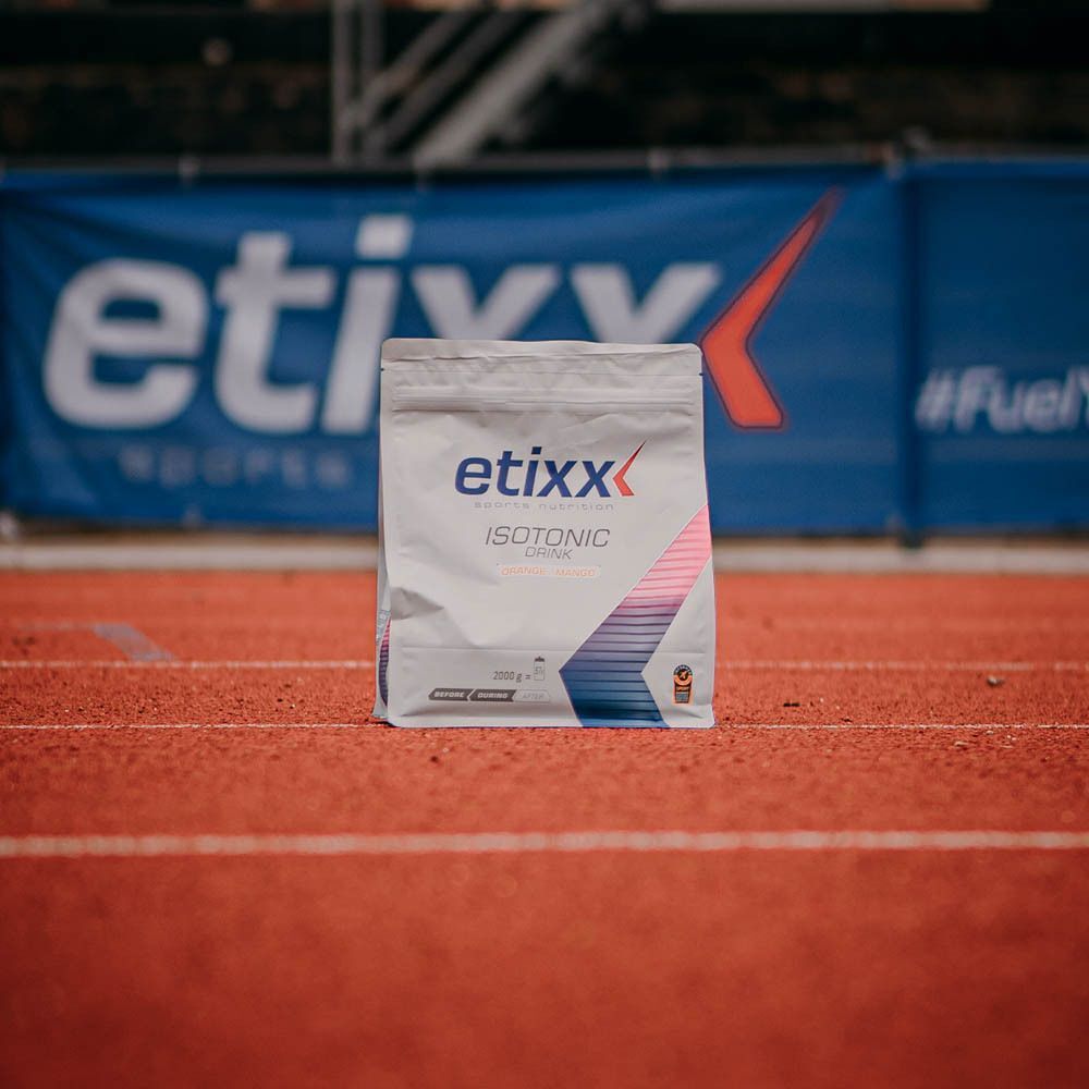Etixx Isotonic Drink Citron zak op rode atletiekbaan. Wit zakontwerp met logo en productnaam. Achtergrond: banner.