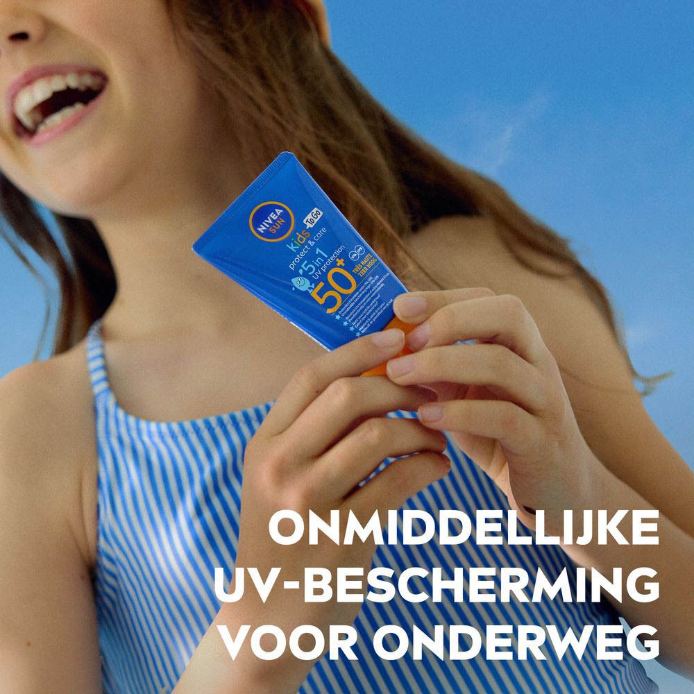 Kind houdt blauwe tube NIVEA Sun Kids To Go vast. Directe UV-bescherming voor onderweg. Blauwe hemel.