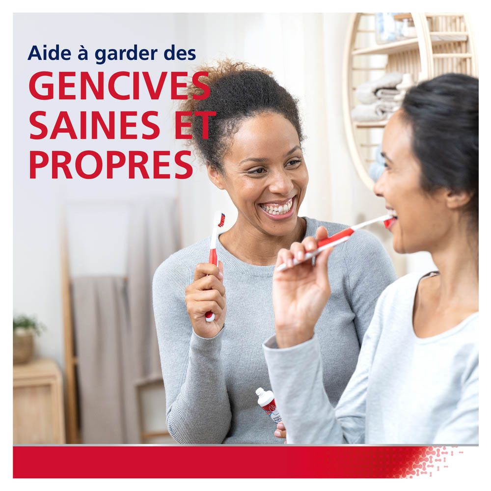 Deux femmes se brossent les dents devant un miroir. Inscription : Aide à garder des gencives saines et propres.