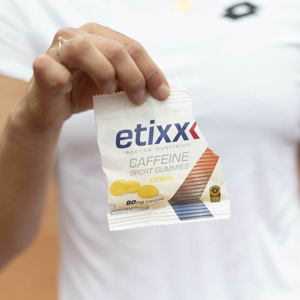 Hand die een zakje Etixx Caffeine Sport Gummies vasthoudt. Wit zakje met productnaam, afbeelding van gele gummies en 80mg cafeïne.