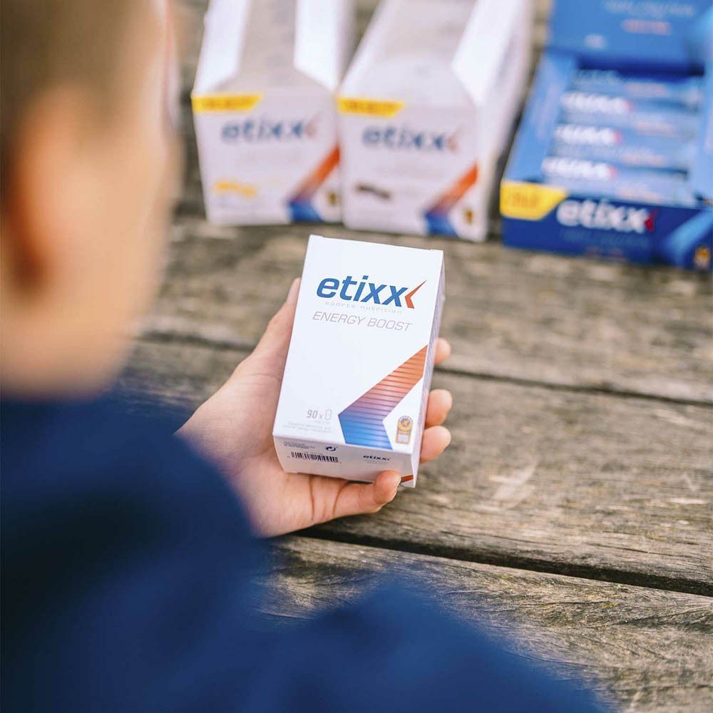 Persoon houdt witte Etixx Energy Boost-doos vast. Meer dozen op de achtergrond.