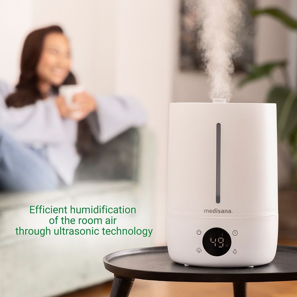 Humidificateur blanc avec affichage numérique. L'appareil porte le logo "medisana" et produit de la vapeur.