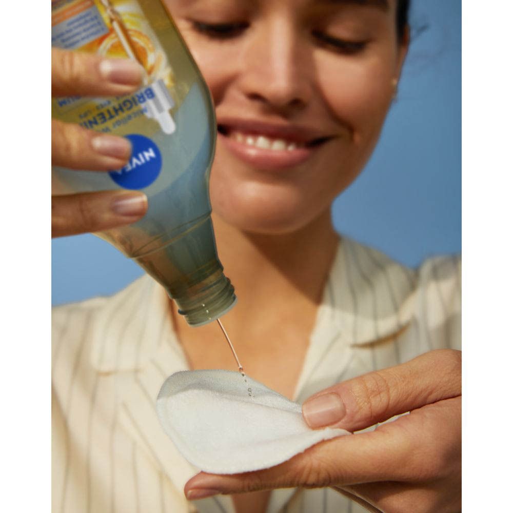 Vrouw druppelt Nivea Skin Glow Micellair Water op een wattenschijfje. Lacht.