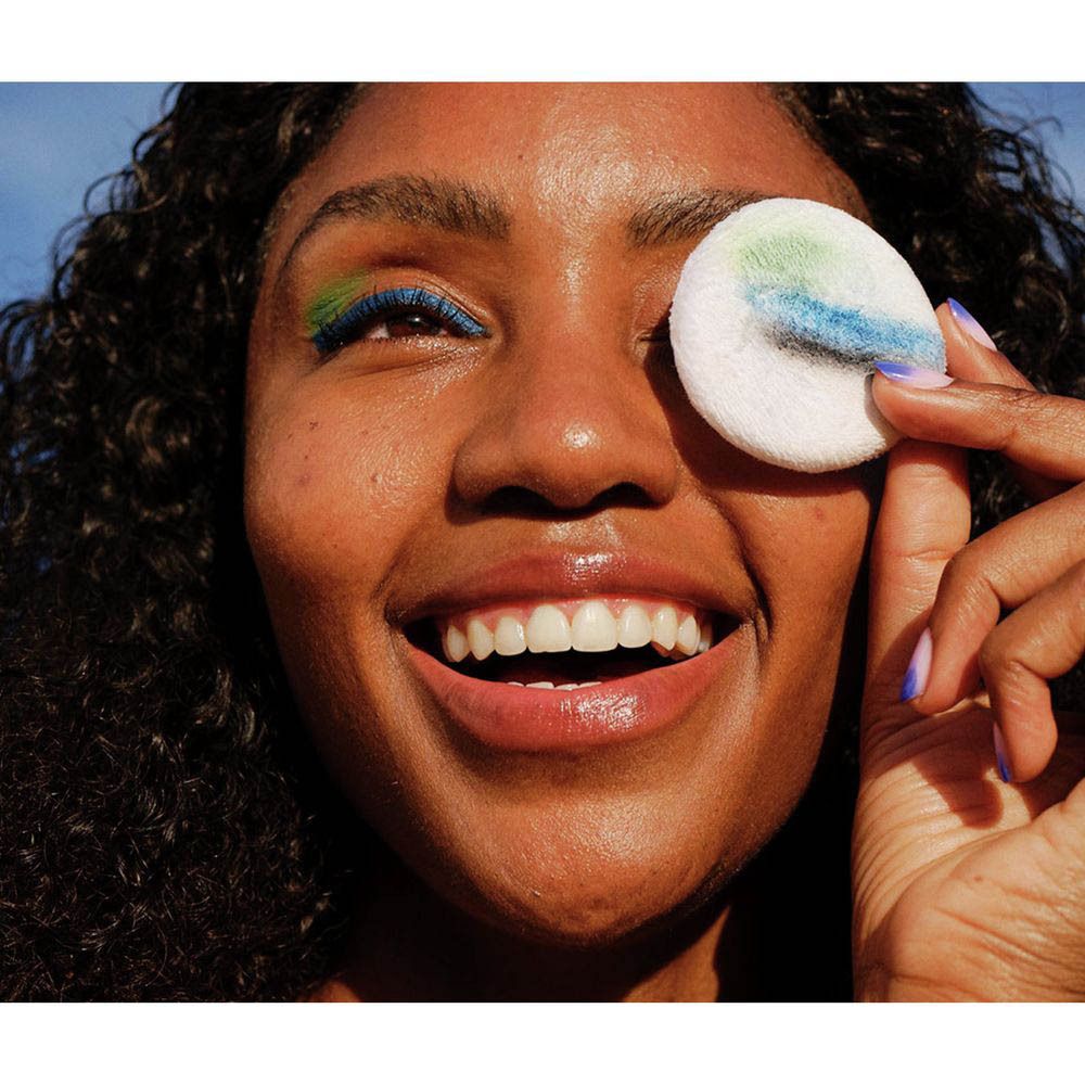 Vrouw met kleurrijke oogmake-up houdt een wattenschijfje met make-upresten voor haar oog. Nivea Skin Glow Micellair Water.