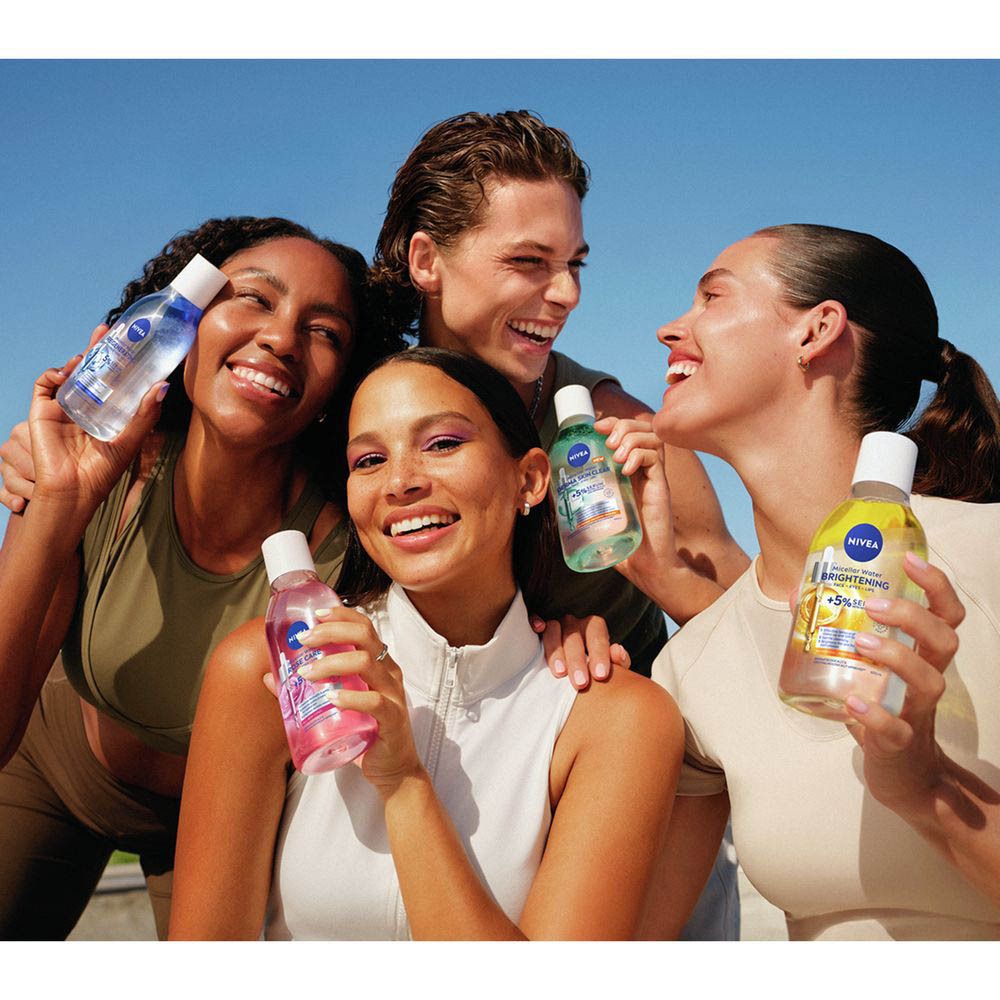 Vier lachende jongvolwassenen houden Nivea Skin Glow Micellair Water flessen vast.