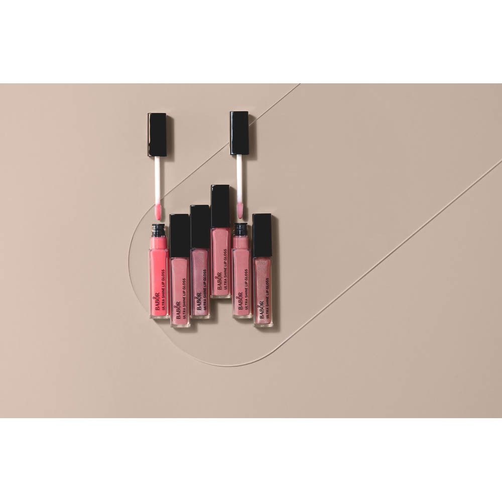 Plusieurs flacons de gloss sur fond beige. Marque et nom du produit visibles.