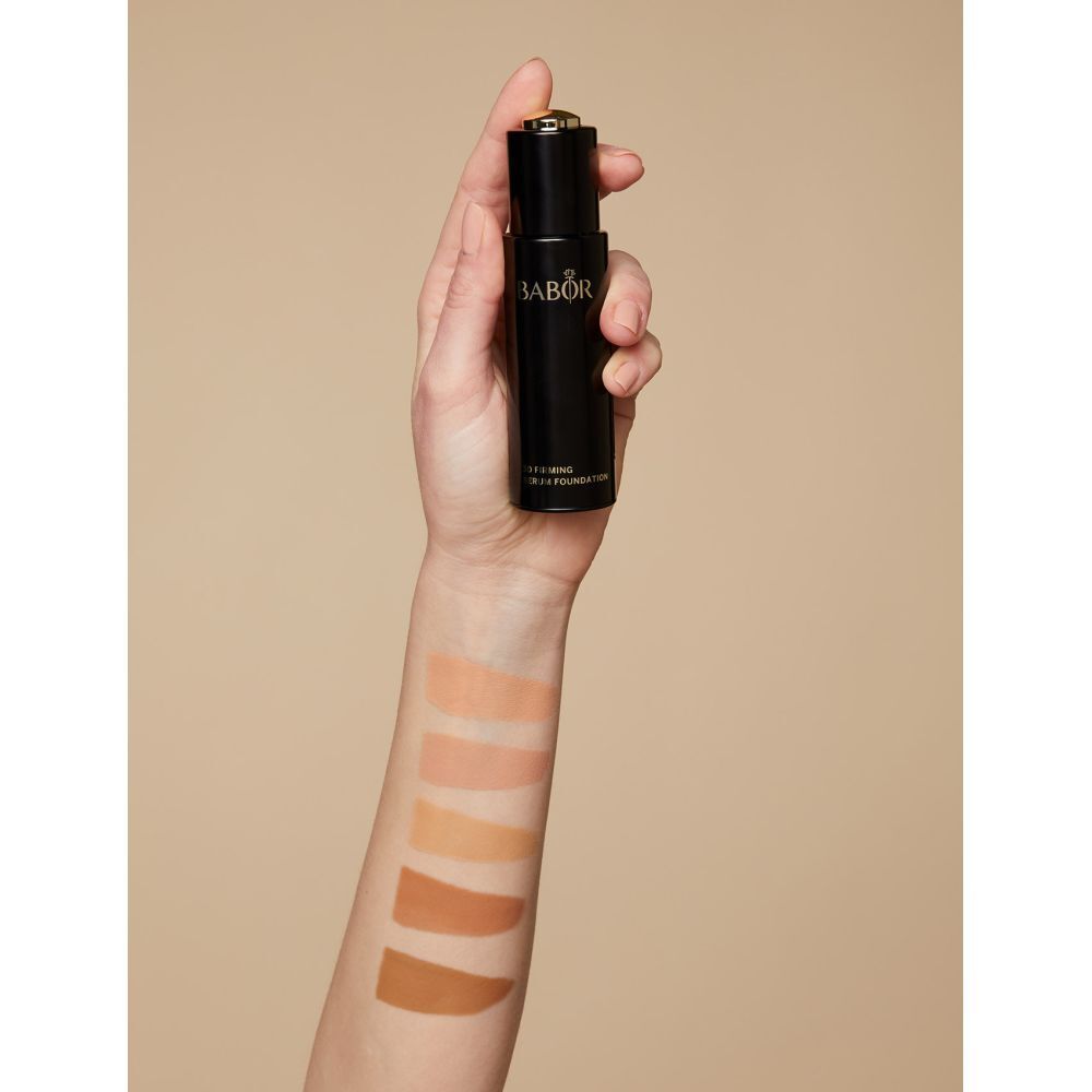 Hand houdt fles vast. Kleurstalen op arm aangebracht. Opschrift: BABOR, 3D Firming Serum Foundation.