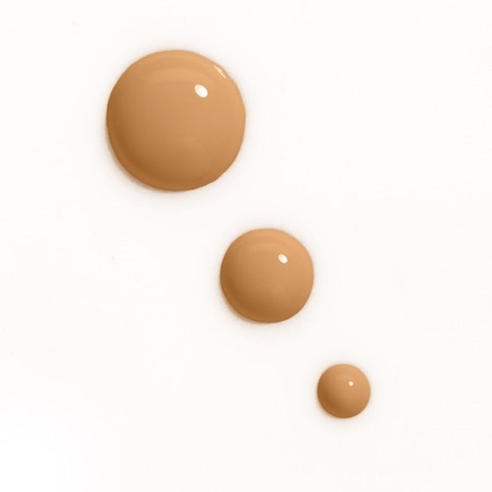 Trois gouttes de fond de teint de différentes tailles sur fond blanc. Teinte : Ivoire.