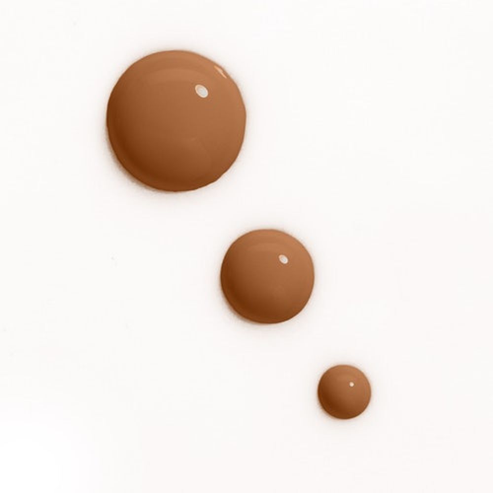 Drie druppels foundation in verschillende maten. Lichte, bruine tinten op witte achtergrond.